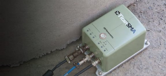 Green accelerometer on the floor of concrete structure with cables connected.