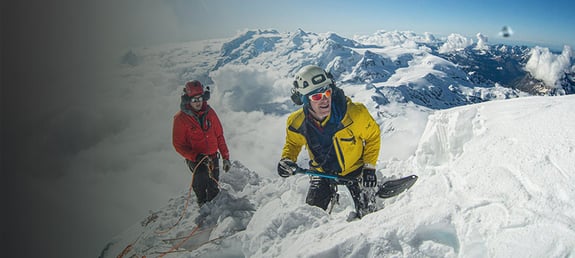 Scientists on top of a mountain digging a hole in the snow for a seismometer