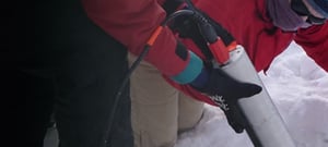 Two scientists lowering a Trillium Cascadia integration kit into a hole in the snow