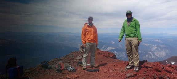 Two scientists standing at the edge of a high cliff with mountains in the distance