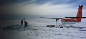 Plane sitting in the snow with scientists setting up seismic equipment nearby