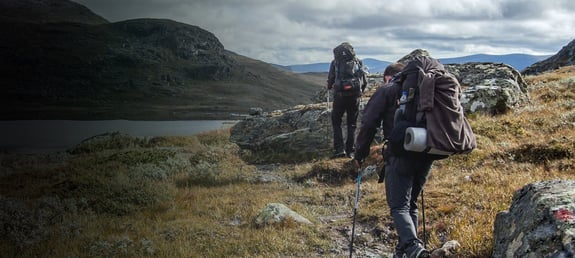 Two scientists hiking with equipment over rocky terrain