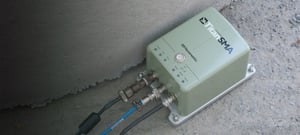 Green Titan SMA accelerometer aligned with a concrete wall connected to 3 cables