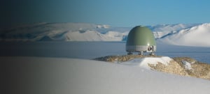 Trillium 360 vault seismometer sitting on large rock in an arctic landscape