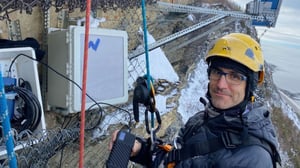 Professor Bernard Giroux in a climbing harness removing seismic data from equipment attached to the cliffside