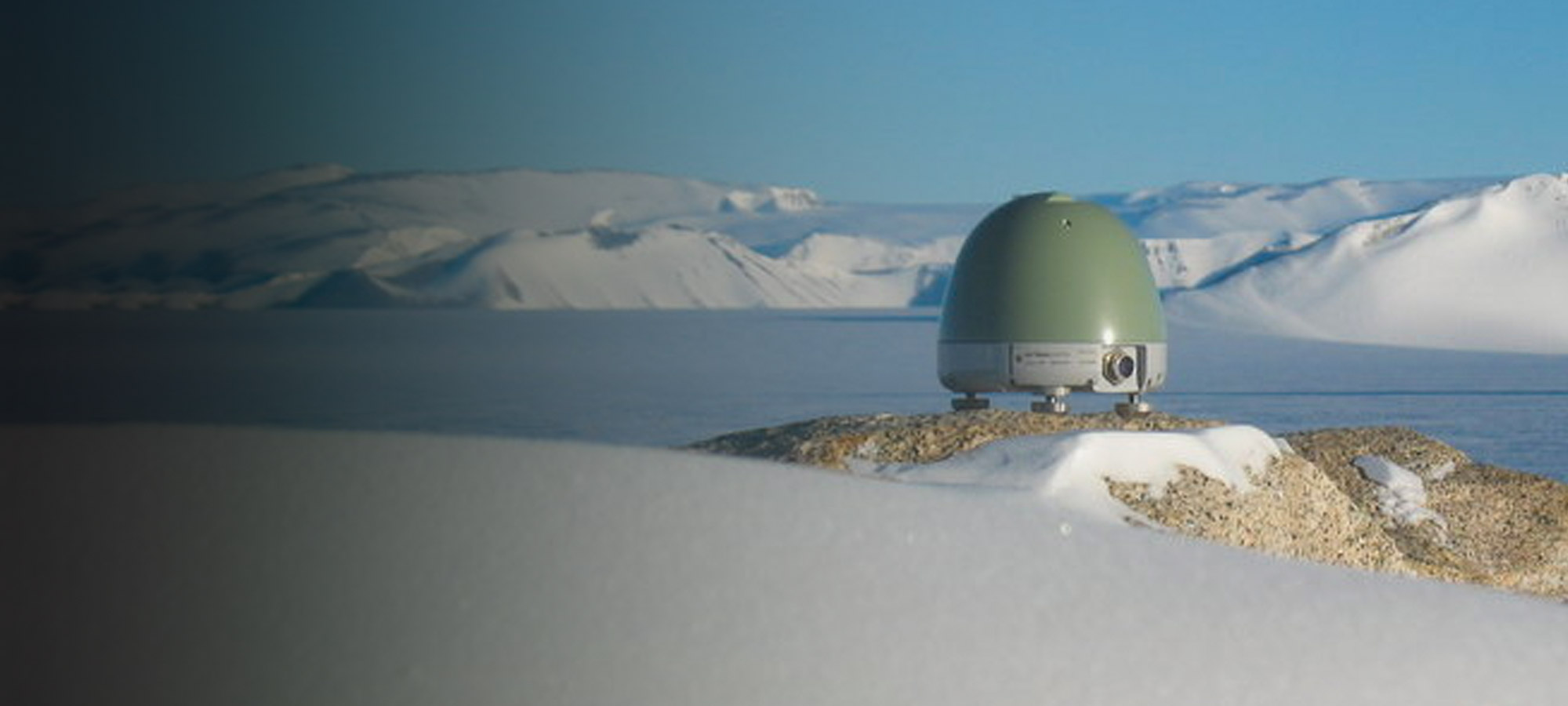 Trillium 360 vault seismometer sitting on large rock in an arctic landscape